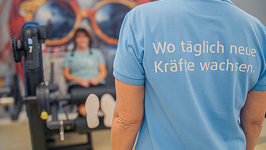 Sportwissen - Monatsthema Trainerin mit hellblauem T-Shirt mit der Aufschrift "Wo täglich neue Kräfte wachsen"